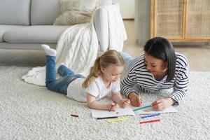 Kid girl daughter and mom drawing painting lying on floor carpet together. Children's education photo