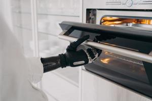 Disabled person opening electric ovens door by bionic prosthetic arm, preparing dinner in kitchen photo