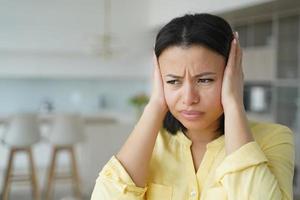 mujer nerviosa molesta que cubre los oídos con las manos que sufren de ruido fuerte del apartamento del vecino foto