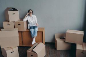 Female calling moving company, orders mover for relocation, sitting with laptop and cardboard boxes photo