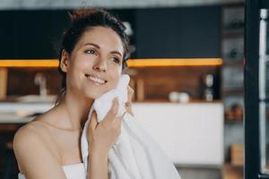 sonriente joven latina limpiando la cara con una toalla de algodón después del lavado matutino. tratamiento de cuidado de la piel foto