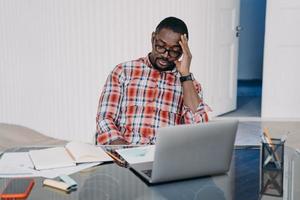 Upset tired african american man sitting at laptop solving working problems. Difficulties in job photo