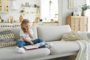 Small kid girl preschooler practices reading fairytale book on sofa at home. Children's education photo