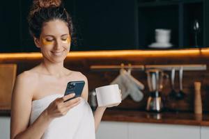 Girl with patches under eyes chatting in social networks, shopping online by phone in the morning photo