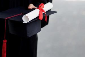 graduación, primer plano estudiante sosteniendo sombrero borla rojo con certificado de diploma en la mano durante el éxito de comienzo graduados de la universidad, grado de ceremonia de felicitación de educación conceptual. foto