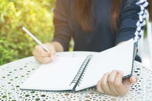 close up hand young woman are sitting on a marble chair. using pen writing Record Lecture note pad into the book in park public photo