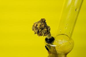 Marijuana bud and bong on yellow background, close up photo