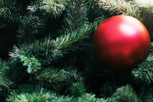 Closeup of red bauble hanging from a decorated christmas tree on blurred of  lights with decorated tree, sparkling and bokeh background. copy space for your text. photo