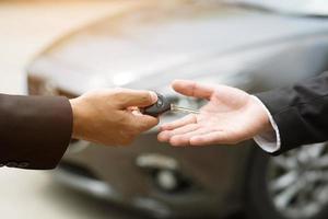 Car key, businessman handing over gives the car key to the other man on car background. photo