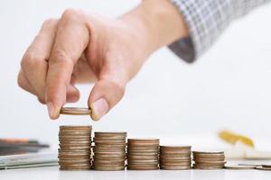 close up hand business man accounting calculator with savings money coins stacked row with hand putting coins in jug glass. concept Write Finance accounting. photo