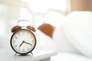 man hates waking up early in the morning. Sleepy girl looking at alarm clock and trying to hide under the pillow photo