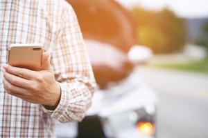 close up businessman hand using a mobile smart phone call a car mechanic ask for help assistance because car broken roadside. people journey friends standing wait beside broken car background. photo