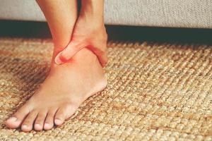 A woman suffering from feeling knee pain sitting sofa at home. hand massaging her painful knee. Health care and medical concept. photo