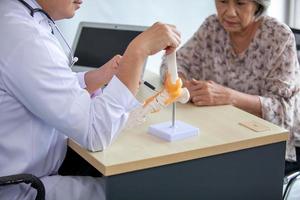 The doctor is explaining to the senior patient the foot pain with model. photo