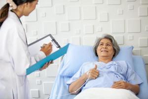 una anciana levanta el pulgar y sonríe mientras el médico examina la condición en la sala de recuperación. concepto de salud y medicina. foto