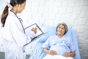 Beautiful asian doctor with stethoscope and document folder, examine the symptom for patient in the recovery room. Healthcare and medicine concept. photo