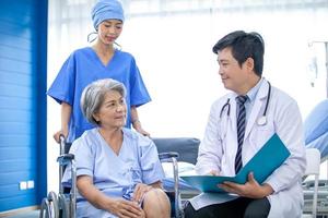 asian doctor with stethoscope and document folder, examine the symptom for senior patient in the recovery room. Healthcare and medicine concept. photo