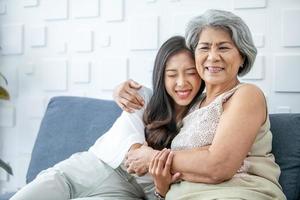 Asian grandma and granddaughter hugged with happy mood on the sofa in home. photo