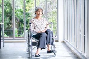 Happy elderly asian woman sitting on wheelchair at home, senior therapy patient at home concept. photo