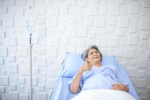 An elderly woman thumbs up and smiling as the doctor examines the condition in the recovery room. Healthcare and medicine concept. photo