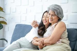 Asian grandma and granddaughter hugged with happy mood on the sofa in home. photo