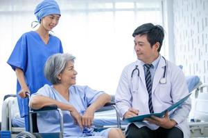 asian doctor with stethoscope and document folder, examine the symptom for senior patient in the recovery room. Healthcare and medicine concept. photo