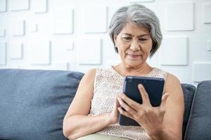 gray haired asian woman is holding smart phone using online apps or shopping online. photo