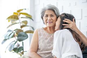 Asian grandma and granddaughter hugged with happy mood on the sofa in home. photo