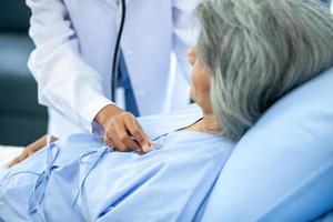 doctor visiting ward have woman patient and check her with stethoscope on bed. Woman patient lying on hospital bed while doctor giving her checkup. photo