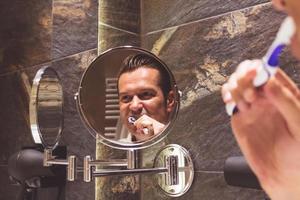 reflejo en un espejo de un hombre cepillando los dientes en el baño. foto