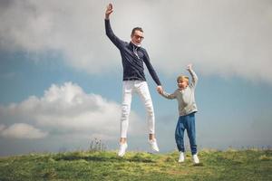 padre e hijo despreocupados saltando sobre un prado contra el cielo. foto