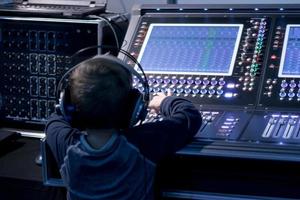 Rear view of boy with headphones editing music in recording studio. photo