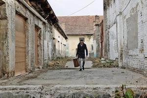 Full length of man with suitcase walking among abandoned buildings. photo