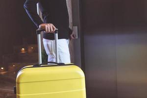 Unrecognizable man with suitcase pressing elevator button in a hallway. photo