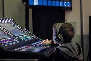 Kid with headphones adjusting volume on audio mixer in recording studio. photo