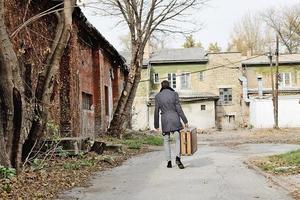 Rear view of man carrying suitcase outdoors. photo