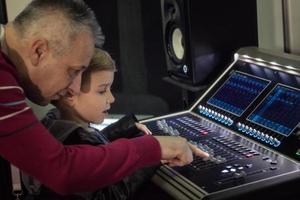 Music producer teaching little boy to edit sound on audio mixer. photo