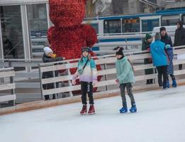 la gente se divierte patinando en una pista de hielo pública construida por el municipio en las calles de la ciudad durante la navidad foto