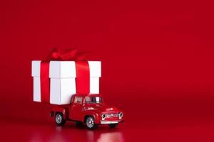 Red car with a gift box on a red background. Concept - delivery of gifts for the holidays, Valentine's Day, International Women's Day, February 14, March 8. Shopping, sale photo