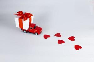 Red car with a gift box on a white background. Concept - delivery of gifts for the holidays, Valentine's Day, International Women's Day, February 14, March 8. Shopping, sale photo