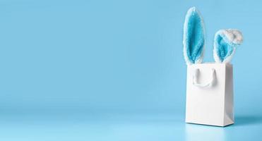 Wide banner on a blue background. The concept of online shopping for Easter, purchases and sale for the holiday. Gift bag with bunny ears photo