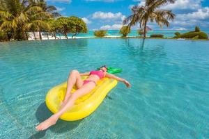 hermosa mujer sexy relajándose en el complejo tropical de la piscina inflable de goma. atractiva mujer delgada despreocupada disfrutando del clima caluroso de verano en bikini rosa. concepto de estilo de vida de ocio de libertad de vacaciones
