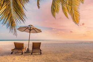 Perfect tropical sunset scenery, two sun beds, loungers, umbrella under palm tree. White sand, sea view with horizon, colorful twilight sky, calmness and relaxation. Inspirational beach resort hotel