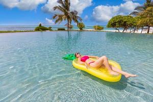 hermosa mujer sexy relajándose en el complejo tropical de la piscina inflable de goma. atractiva mujer delgada despreocupada disfrutando del clima caluroso de verano en bikini rosa. concepto de estilo de vida de ocio de libertad de vacaciones