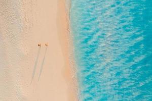 Aerial view of amazing beach with couple walking in sunset light close to turquoise sea. Top view of summer beach landscape, romantic inspirational couple vacation, romantic holiday. Freedom travel photo