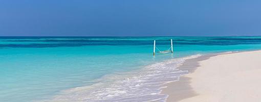 Luxury beach. Luxurious travel background. Summer vacation or holiday concept on tropical beach, white sand and an amazing over water hammock over blue sea with horizontal view. Exotic holiday resort photo