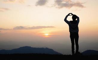 manos en forma de corazón de amor, manos femeninas en forma de corazón contra el cielo pasan rayos de sol. feliz en el amor foto