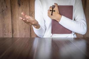 Woman praying while holding Bible and cross, Pray in the Morning , Woman praying with hands together on the Sunrise background. photo