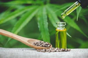 Hemp seeds and  droplet dosing a biological and ecological hemp plant herbal pharmaceutical cbd oil from a jar on a green marijuana leaf background.  medical marijuana concept, CBD cannabis OIL. photo