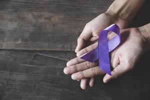 mano de mujer sosteniendo cinta morada, concepto de mes de concientización sobre violencia doméstica con cinta de concientización de color púrpura oscuro. foto